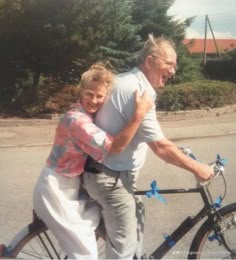 an older man and woman riding on the back of a bicycle