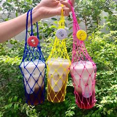 three different colored cups are hanging from a wire basket in front of some bushes and trees