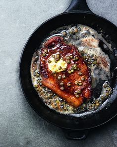 a skillet filled with meat and vegetables on top of a gray countertop next to a knife