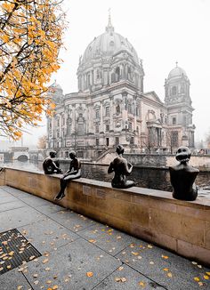 three statues sitting on the edge of a wall next to a body of water with a building in the background