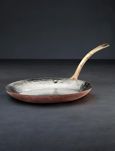 a silver and copper pan with a spoon in it on a black tablecloth background