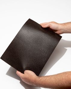 a person holding up a black piece of leather on a white surface with one hand