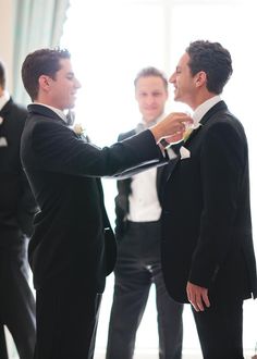 two men in tuxedos standing next to each other and one is fixing his bow tie