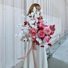 a woman holding a bouquet of flowers in front of a white wall with pink and red accents