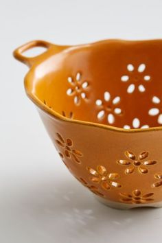 an orange bowl with flowers on the side and holes in the bottom, sitting on a white surface