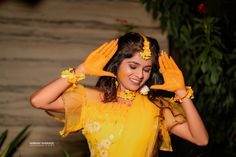 a woman in yellow is smiling and holding her hands up to her head with both hands