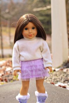 the doll is wearing a purple skirt and white sweater with fuzzy boots on it's feet