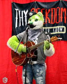 a man in a costume playing a guitar and singing into a microphone while wearing an animal mask