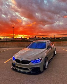 a silver car parked in a parking lot under a red and orange sky with clouds