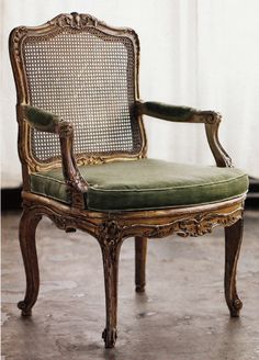 an antique chair with green cushions and caned back, in front of a white wall