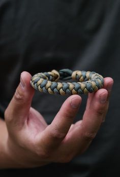 a person holding up a bracelet in their hands with two different colored braids on it