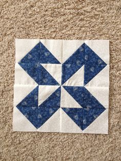 a blue and white quilted block with an arrow in the center on a tan carpet