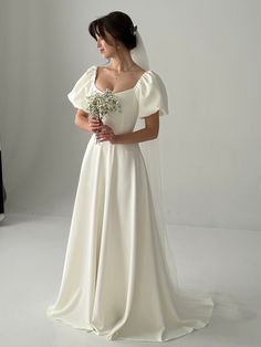 a woman in a white wedding dress holding a flower bouquet and looking off to the side