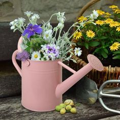 a pink watering can filled with flowers next to a basket of yellow and purple flowers