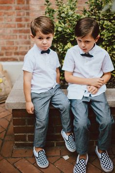 two young boys sitting next to each other on top of a brick bench wearing matching shoes