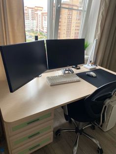 a computer desk with two monitors and a keyboard on it in front of a window