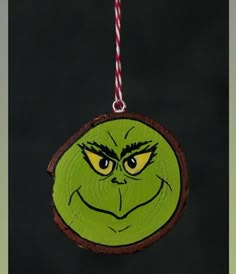 a green ornament with an evil grin face on it's side hanging from a red and white string