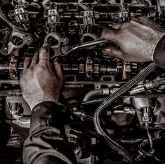 a man working on an engine in black and white with his hands holding the hose