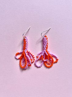 an orange and purple beaded octopus earrings on a pink background with silver earwires