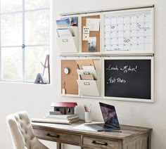 a wooden desk topped with a laptop computer next to a wall mounted chalkboard and calendars