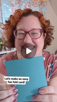 a woman with red hair and glasses making a funny face while holding a blue piece of paper