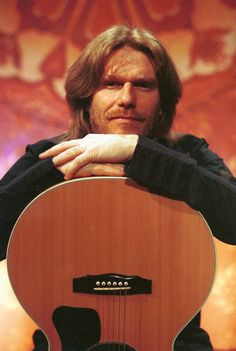 a man holding an acoustic guitar with his hands on the top of its head and looking at the camera