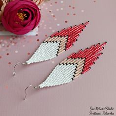 two pairs of beaded earrings sitting on top of a table next to a flower