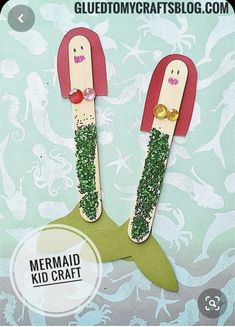 two little mermaids made out of popsicle sticks with glitter on them, sitting next to each other