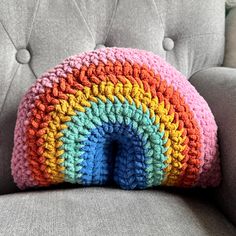 a crocheted rainbow pillow sitting on top of a gray couch