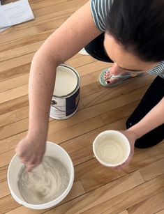 a woman sitting on the floor with two buckets of paint in front of her