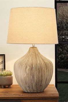 a table lamp sitting on top of a wooden table next to a potted plant