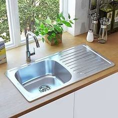 a stainless steel sink in a kitchen next to a window with green plants on it