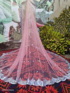 a pink wedding veil with sequins on the bottom is displayed in front of a painting