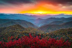 the sun is setting over the mountains in the fall season with red foliage on the foreground