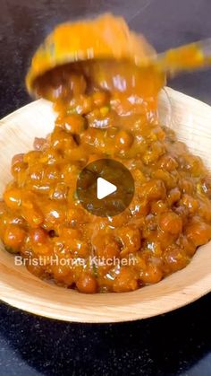 a wooden bowl filled with food on top of a black counter next to a spoon