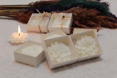 four white boxes with flowers on them next to a lit candle and some dried grass