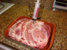 raw meat in an orange pan on a kitchen counter with a bottle of ketchup next to it