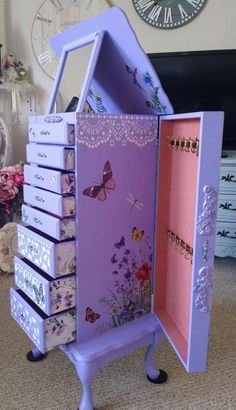 a purple doll house with drawers and butterflies on the doors is shown in front of a wall clock