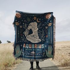 a person standing on a dirt road holding up a blanket that says capricorn