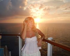 a woman standing on the deck of a cruise ship looking at the sun setting over the ocean