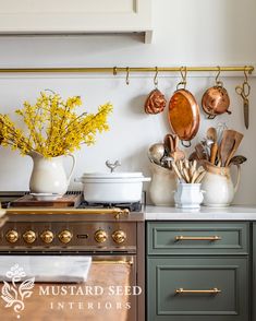 pots and pans are hanging on the wall above an oven in a kitchen with green cabinets