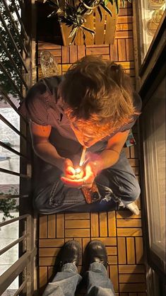 a man sitting on the floor holding a lit candle in his hand while looking down