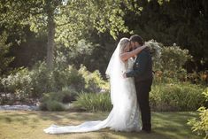 a bride and groom standing in front of some trees with their arms around each other