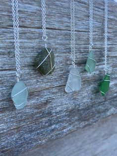 four sea glass necklaces hanging on a wooden board