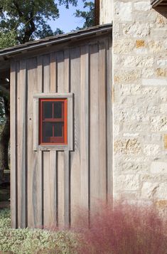 a small wooden building with a red window in it's side door and brick wall