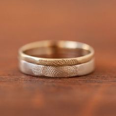 two wedding bands with fingerprints on them sitting on top of a wooden table