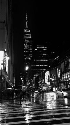 a black and white photo of a city street at night with people crossing the street