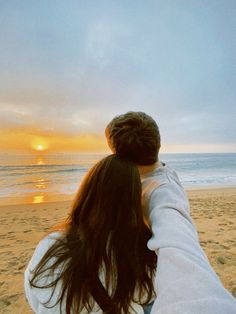 two people holding hands on the beach at sunset