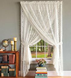 a living room with bookshelves and a window covered in white lace curtain panels