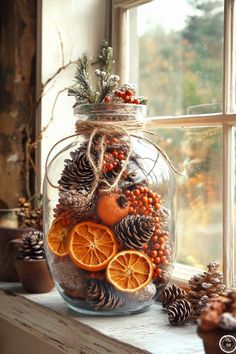 a glass jar filled with oranges and pine cones sitting on top of a window sill